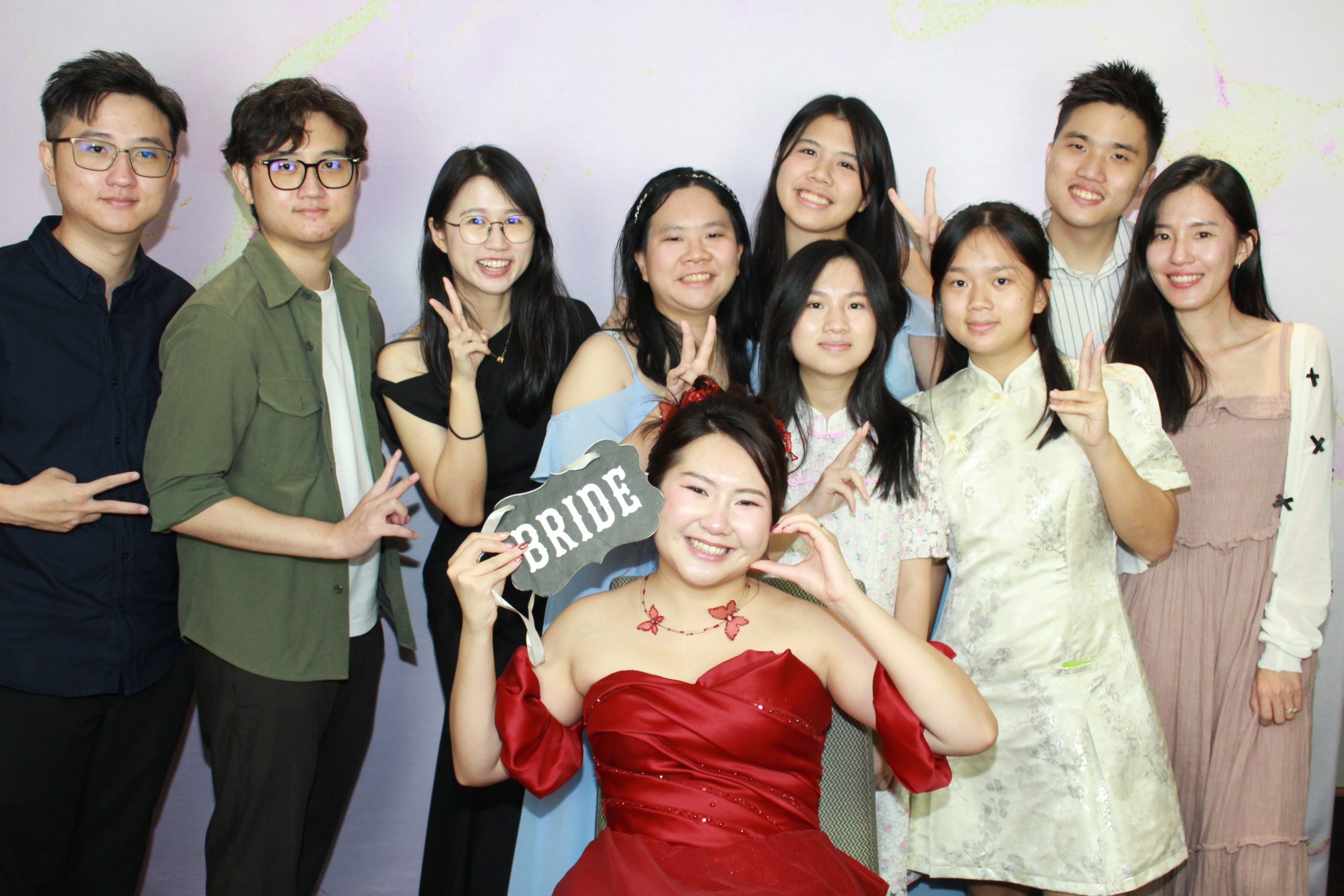 Bride in a red dress posing with wedding guests and a Bride photo booth sign