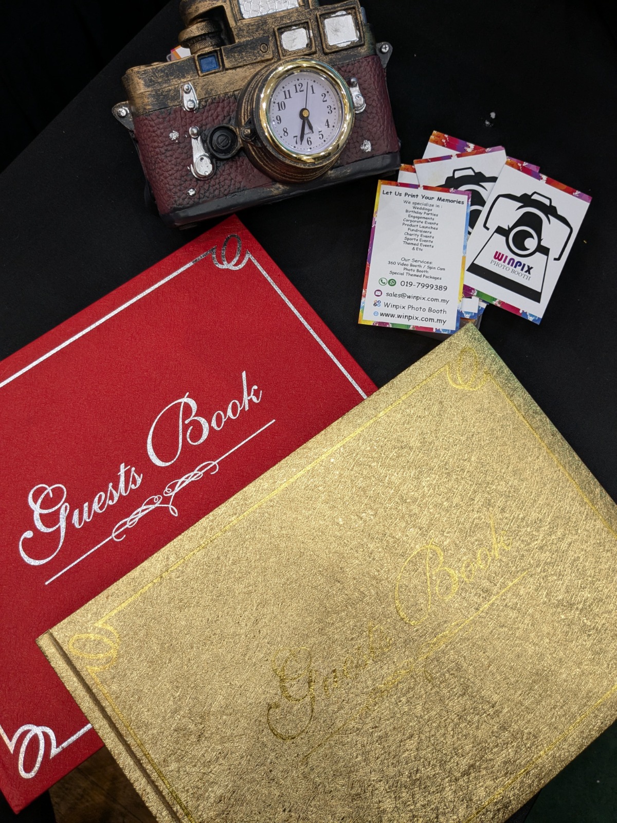 Red and gold guest book covers beside Winpix Photo Booth cards and a camera-shaped clock